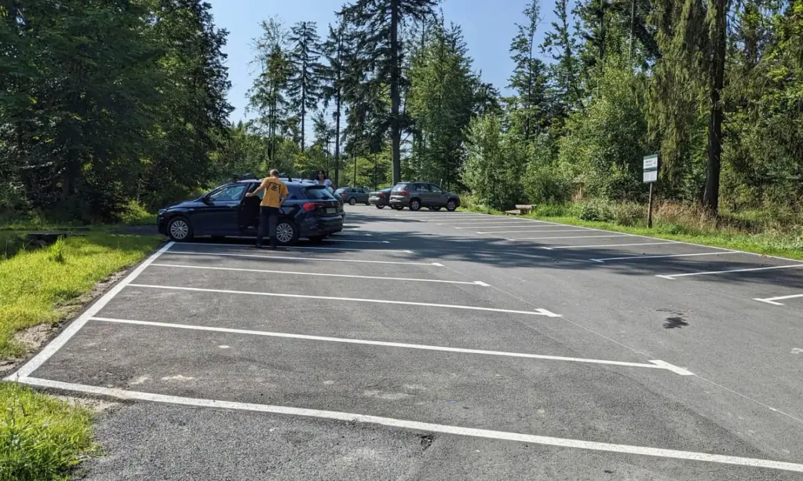 Parking przy szlaku na przełęcz Szarcula. Kilka samochodów na nowym, asfaltowym parkingu otoczonym lasem.