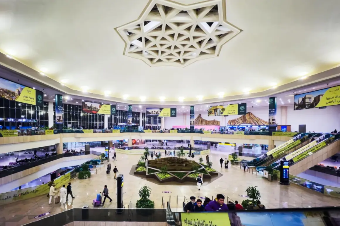 Wnętrze lotniska, które może być największym lotniskiem na świecie, z wielopoziomowymi galeriami, schodami ruchomymi i centralną zieloną przestrzenią.