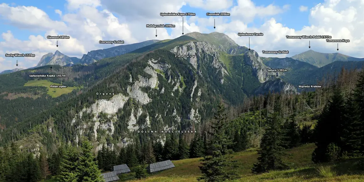 Widok na Tatry z Doliną Kościeliską. W oddali szczyty: Giewont, Ciemniak, Tomanowy Wierch Polski. Na pierwszym planie widać drewniane hale stoły.