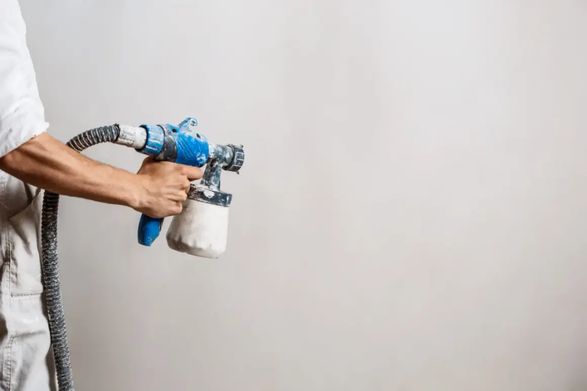 Main tenant, prêt à peindre. Le pistolet à peinture, avec son réservoir rempli, attend la dilution parfaite pour un travail impeccable.