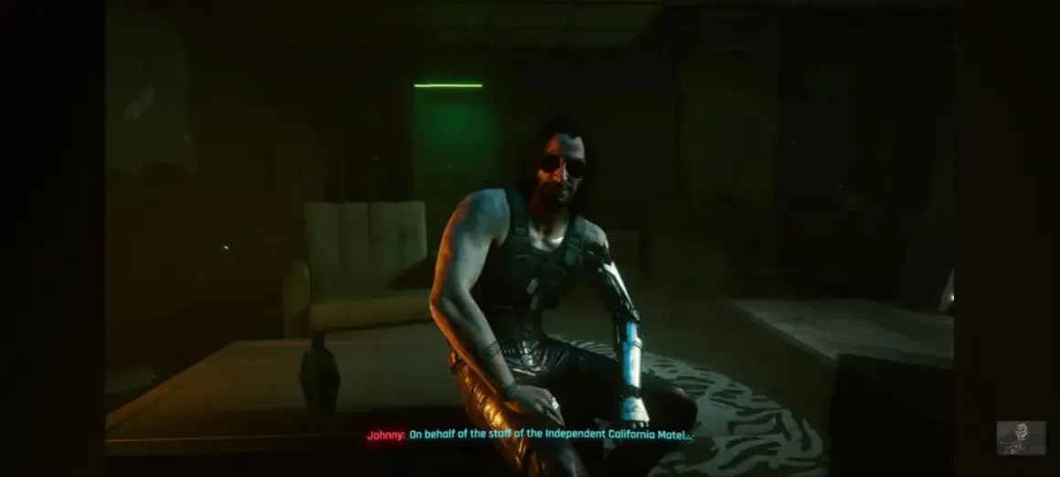 Johnny Silverhand z Cyberpunk 2077 w mrocznym pokoju, z cybernetycznym ramieniem i w okularach przeciwsłonecznych.
