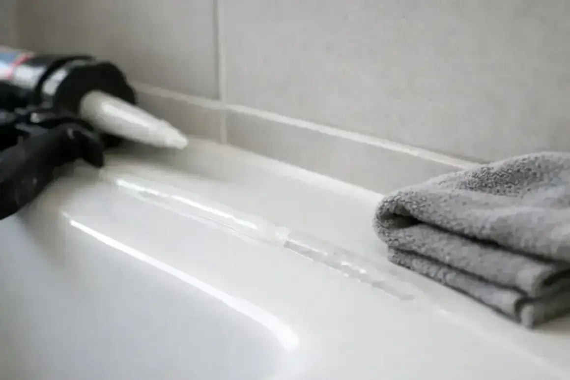Pistolet do silikonu i szara ściereczka obok świeżo nałożonej spoiny. Czekamy, aż silikon schnie.