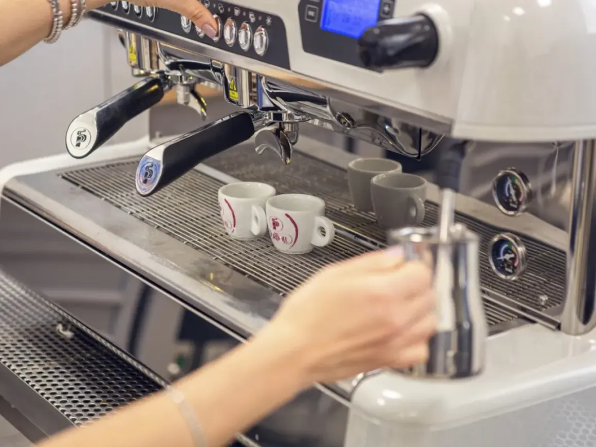 Mano che prepara un caffè con la bar macchina caffè. Due tazzine bianche attendono il loro turno.