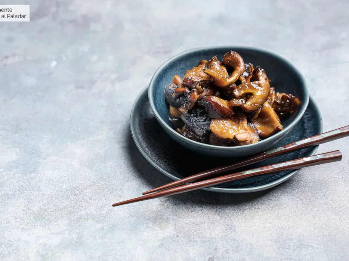 Deliciosas setas shiitake salteadas en un cuenco azul, listas para ser disfrutadas con palillos.