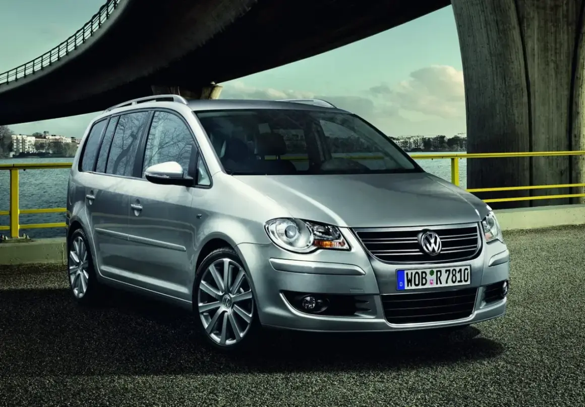 Srebrny, bezawaryjny minivan Volkswagen Touran stoi nad wodą pod mostem.