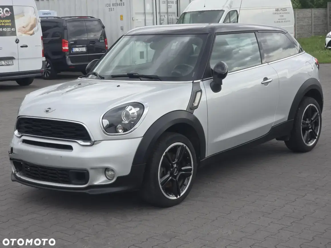 Srebrny mini paceman z czarnym dachem i felgami, zaparkowany na placu.
