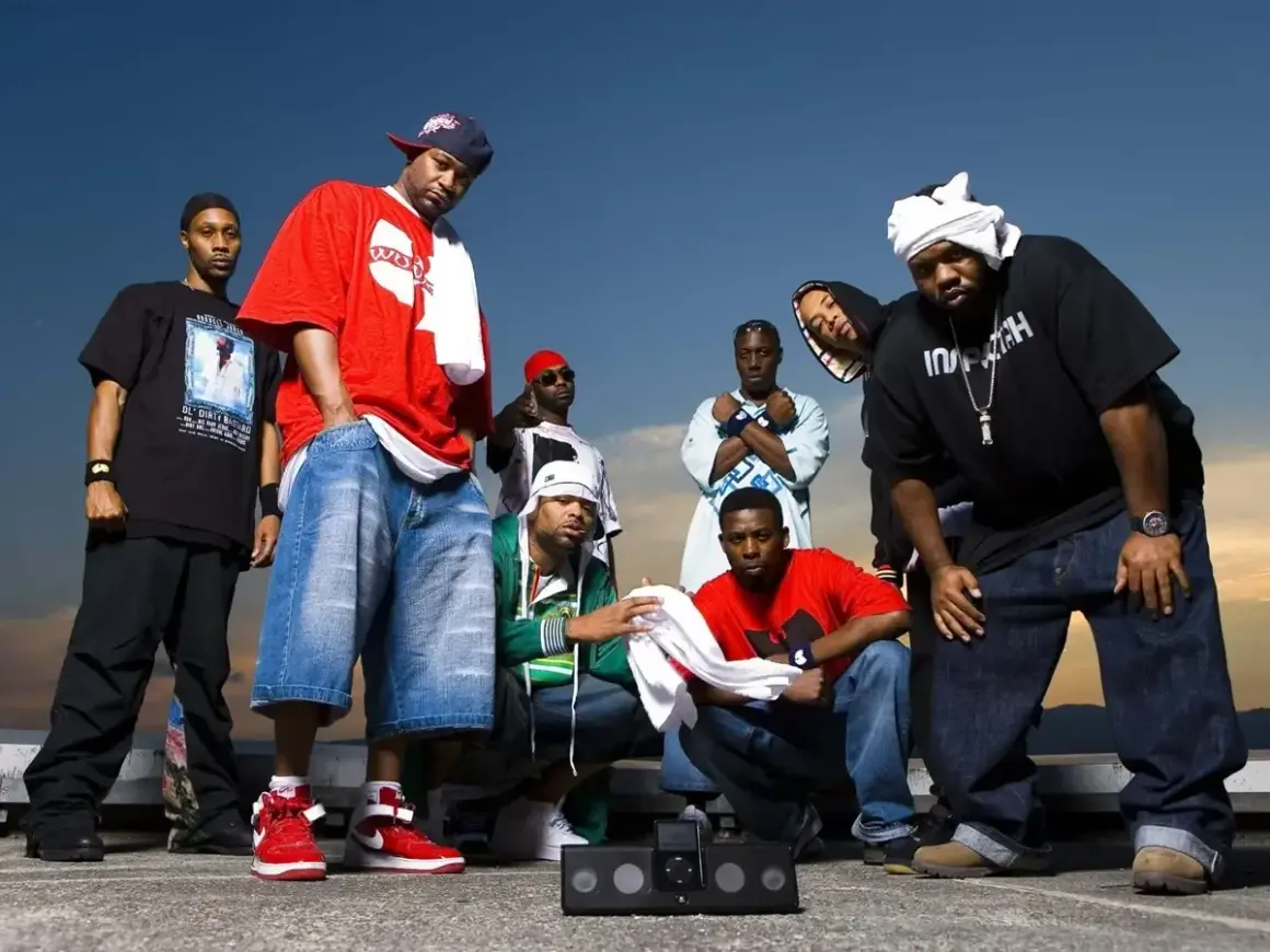 Grupa raperów z Wu-Tang Clan pozuje do zdjęcia na tle nieba.