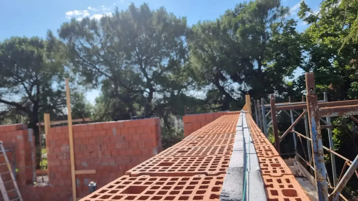 Costruzione di una muratura portante in laterizio, con mattoni forati rossi e blocchi in cemento.