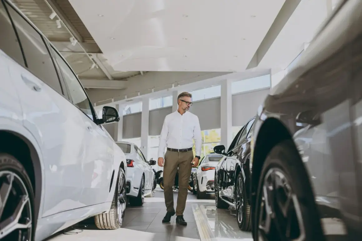 Elegancki mężczyzna w okularach wybiera nowe auto do miasta w salonie samochodowym. Wokół lśniące pojazdy.