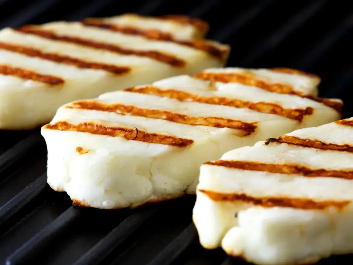 Trzy kawałki halloumi z grilla, z charakterystycznymi brązowymi paskami, leżą na czarnej, żebrowanej powierzchni.