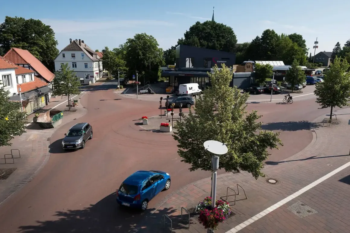 Ein sonniger Tag im **shared space Bohmte**. Autos fahren durch den Kreisverkehr, ein Radfahrer genießt die Fahrt.