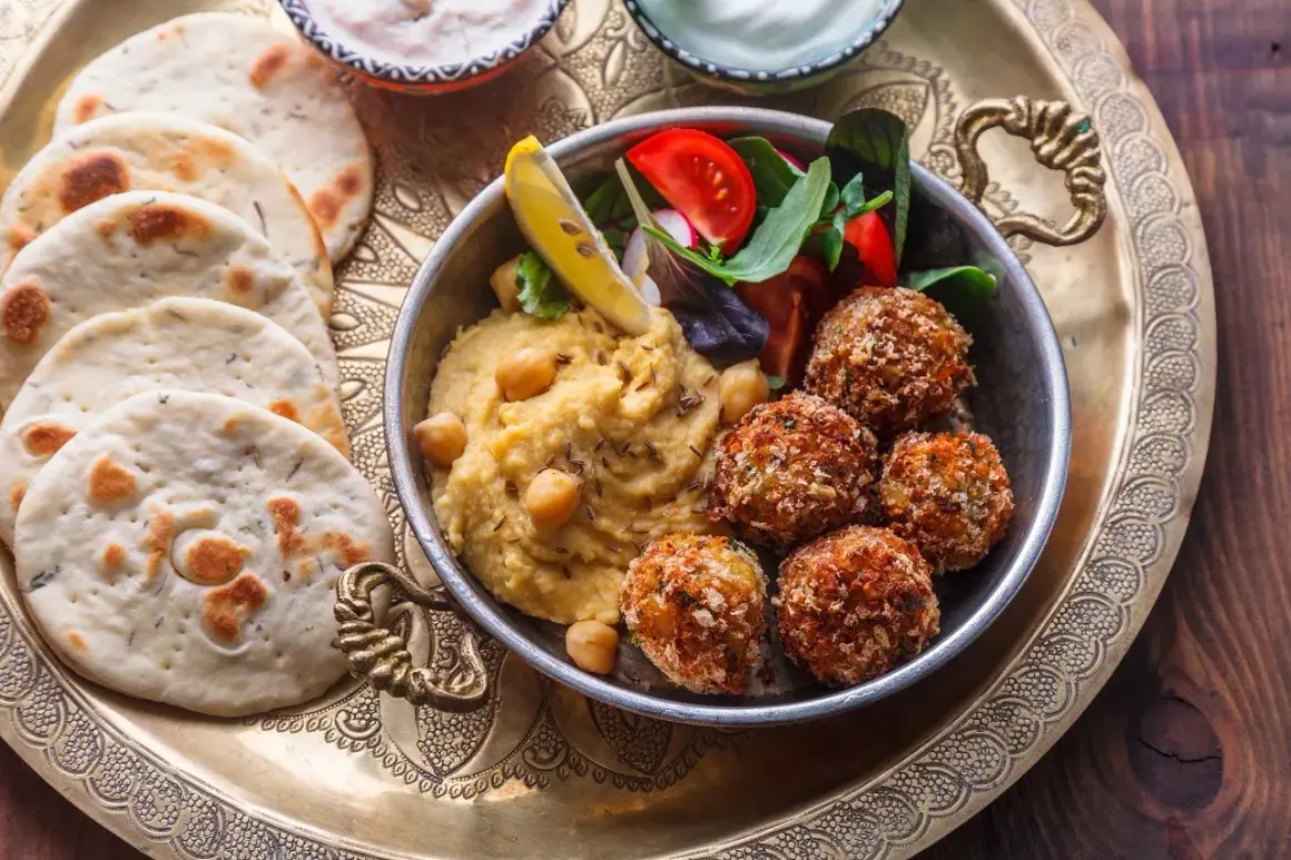 Pyszne jedzenie koszerne: hummus, falafel, świeże pieczywo i sałatka na ozdobnej tacy.