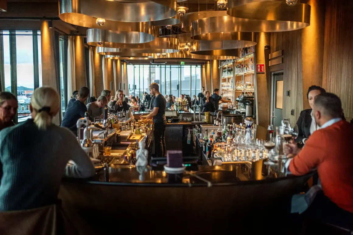 Människor sitter vid en bar med många flaskor och glas. Belysningen är varm och stämningen inbjuder till att läsa **spesso recensioner** om stället.