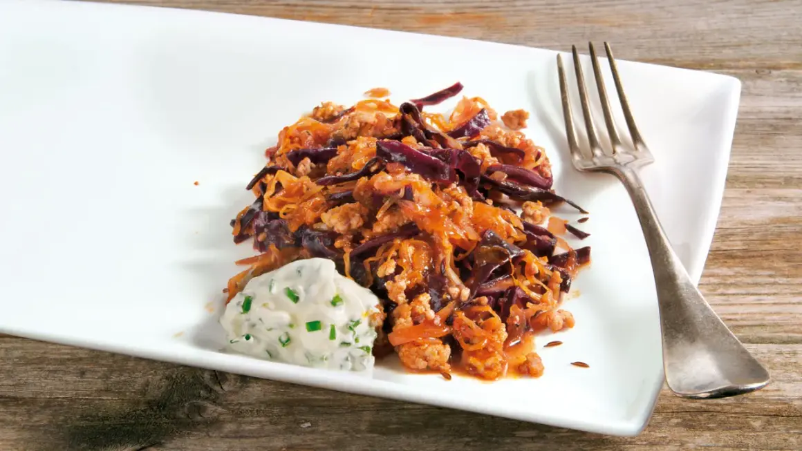 Herzhafte Krautpfanne mit Hackfleisch, serviert mit einem Klecks Kräuterquark und einer Gabel auf einem weißen Teller.