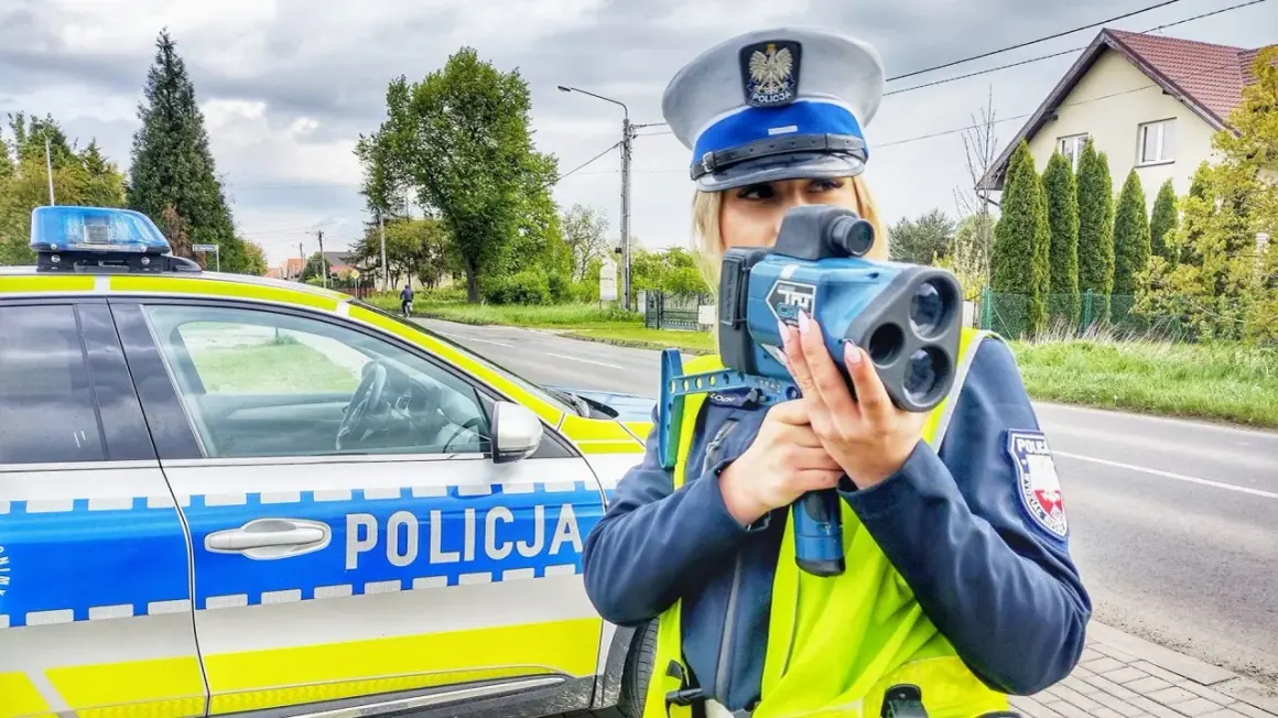 Policjantka z radiowozem i taryfikatorem mierzy prędkość na drodze.