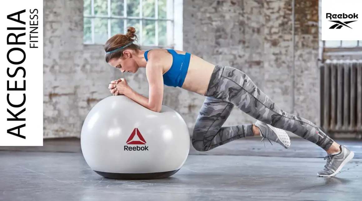 Kobieta w sportowym stroju wykonuje ćwiczenie w podporze na piłce Reebok.