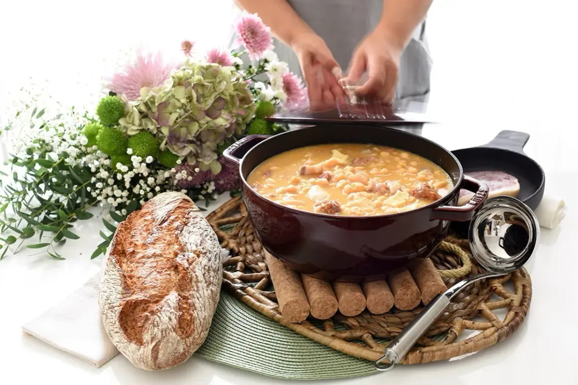 Un reconfortante plato de callos a la gallega humea en una cazuela, acompañado de pan rústico y un ramo de flores.