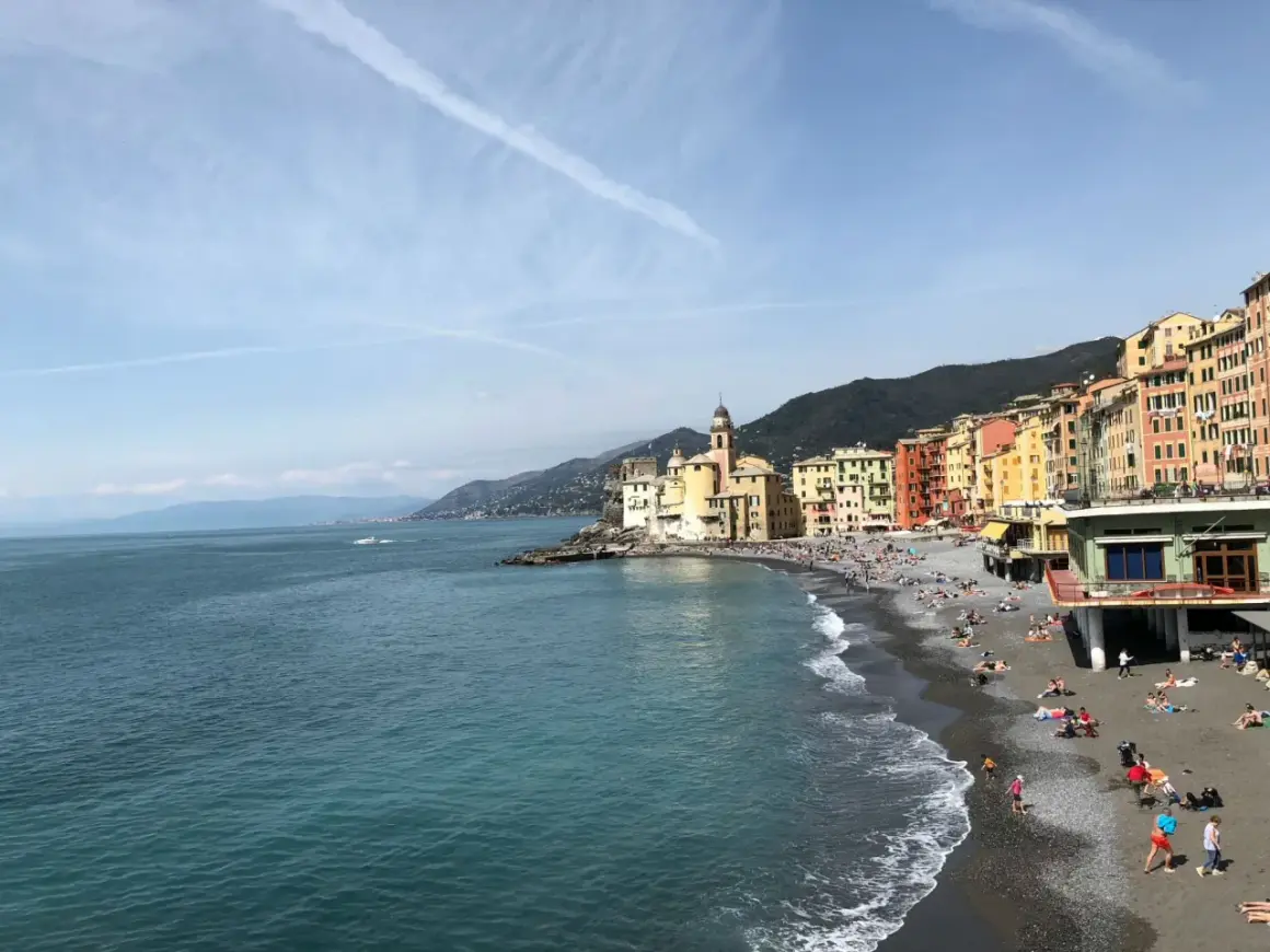 Un angolo di **mare vicino Milano**, con case colorate affacciate su una spiaggia di ciottoli e gente che prende il sole.