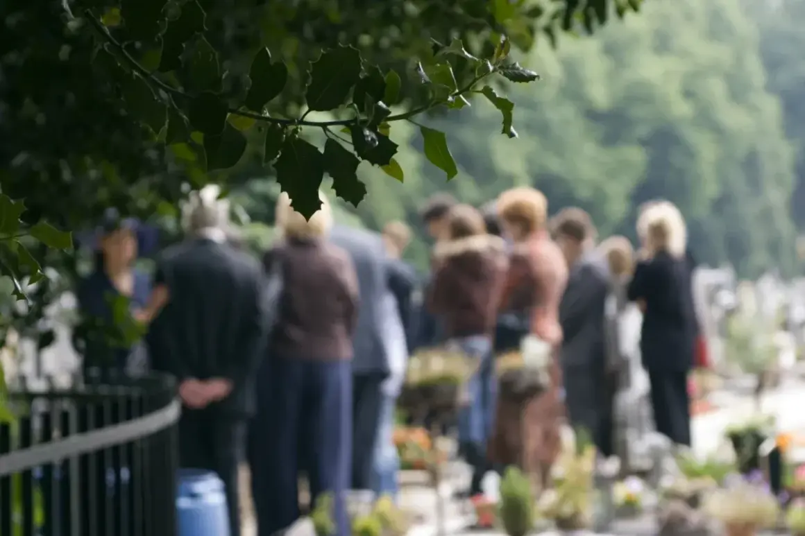 Ludzie na cmentarzu, w zadumie. Czy można pochować zmarłego w innym mieście? Pytanie, które zadaje sobie wielu.