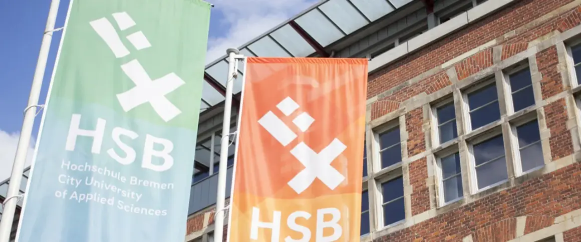 Zwei Fahnen der Hochschule Bremen City University of Applied Sciences wehen vor einem Backsteingebäude.
