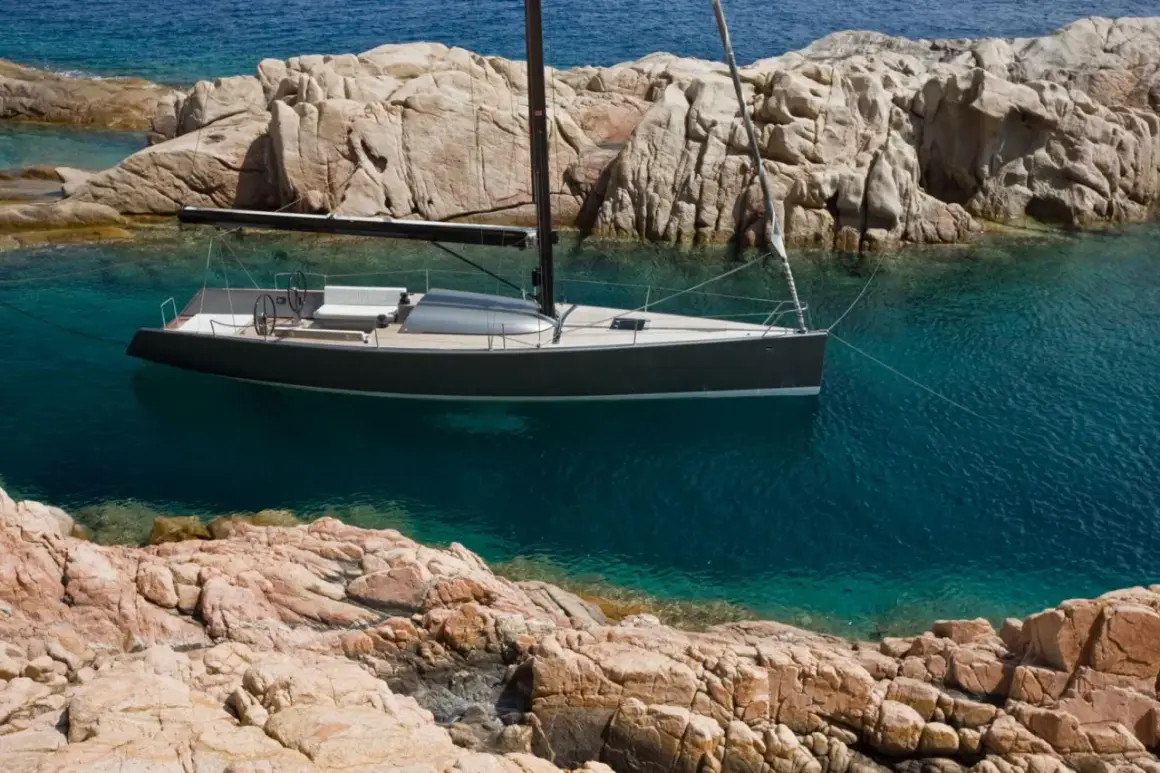 Un elegante yacht Brenta naviga in acque cristalline, ormeggiato tra scogliere rocciose.