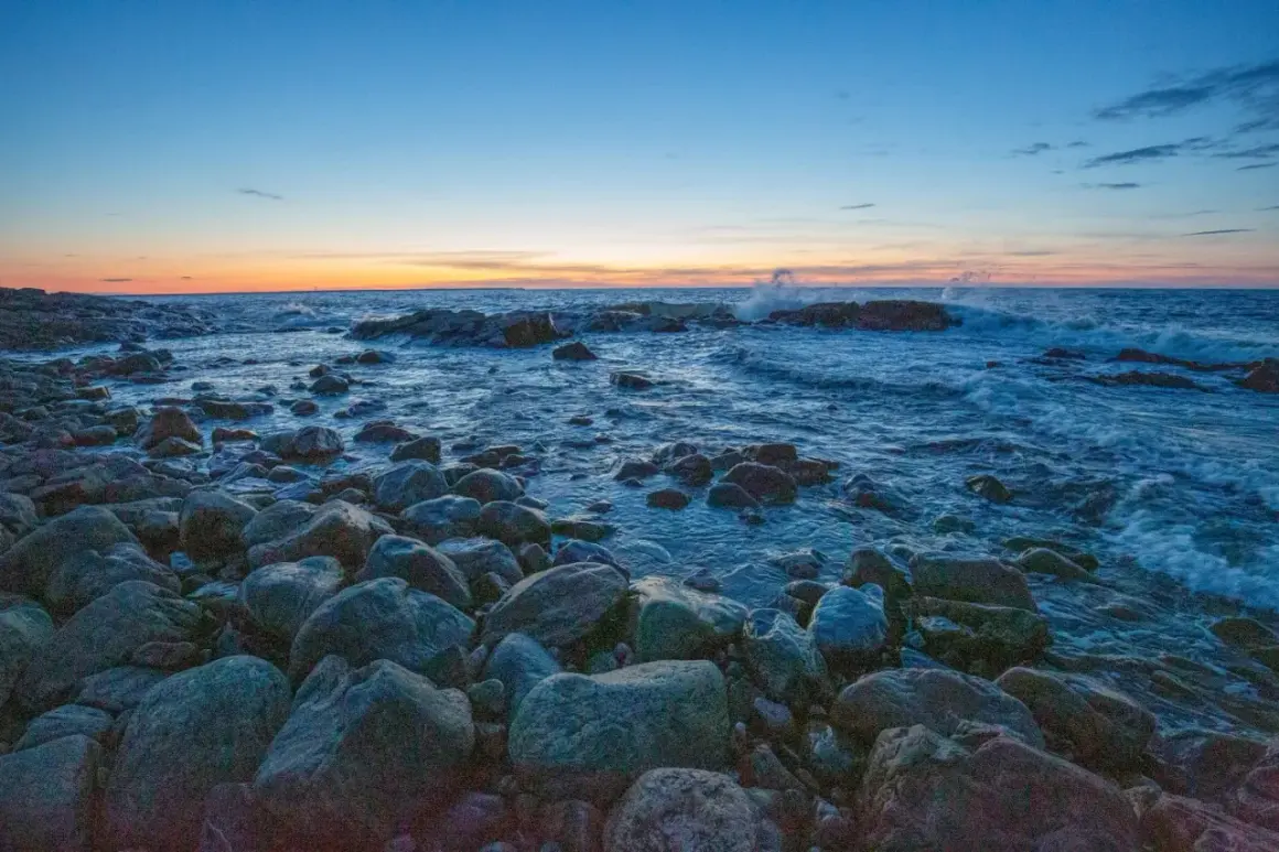 Stenstrand vid solnedgången. Vågor slår mot klipporna i det blåa vattnet. En lugn kväll, precis som det iso betyder.