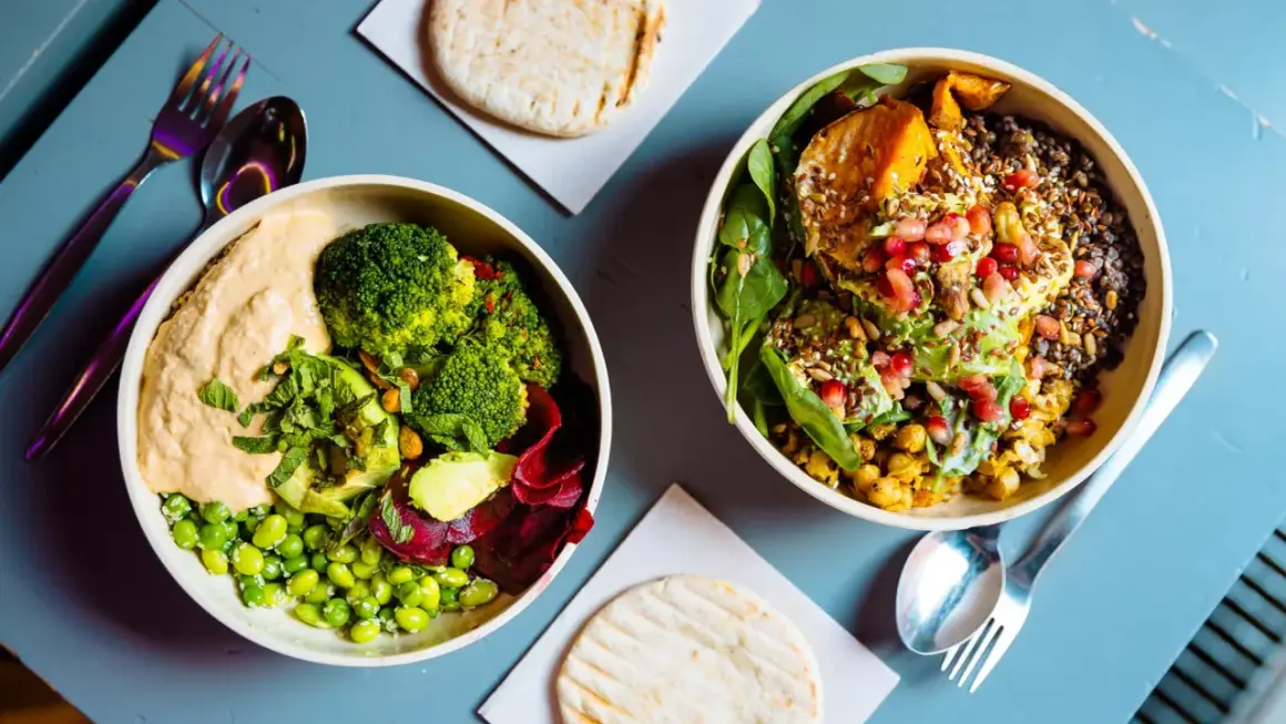 Gesundes Essen nach dem Joggen: Zwei bunte Bowls mit Hummus, Brokkoli, Edamame, Rote Bete, Süßkartoffel, Linsen und Granatapfelkernen.
