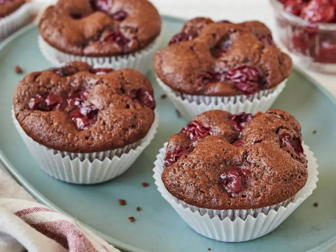 Schoko Kirsch Muffins auf einem blauen Teller, mit Kirschen garniert. Ein Genuss für jeden Schokoladenliebhaber.