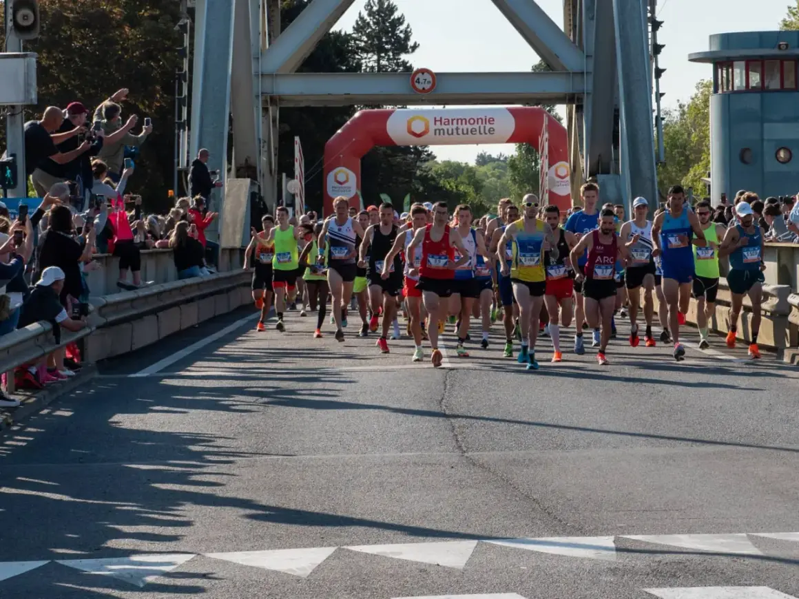 Coureurs au départ du semi-marathon Paris 2026, sous une arche Harmonie Mutuelle. Le soleil brille, les spectateurs encouragent.