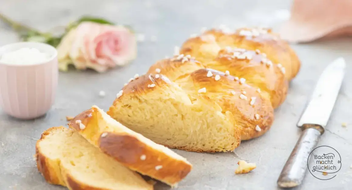 Ein goldbrauner Hefezopf, bestreut mit Hagelzucker, liegt angeschnitten auf grauem Untergrund. Ein tolles Rezept für Hefezopf!