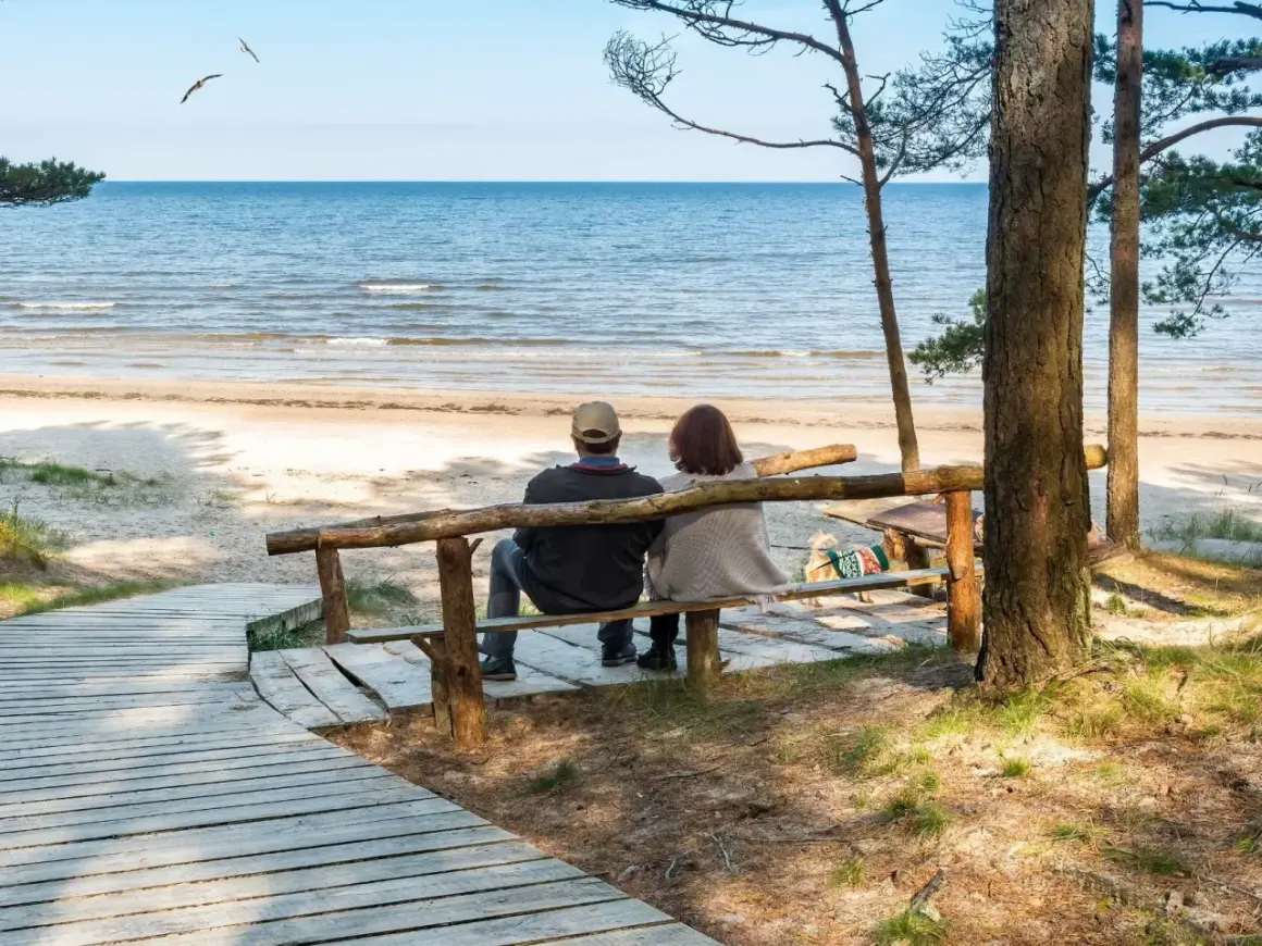 Para odpoczywa na ławce przy plaży, ciesząc się widokiem morza. Idealne miejsce na relaks w sanatorium nad morzem.