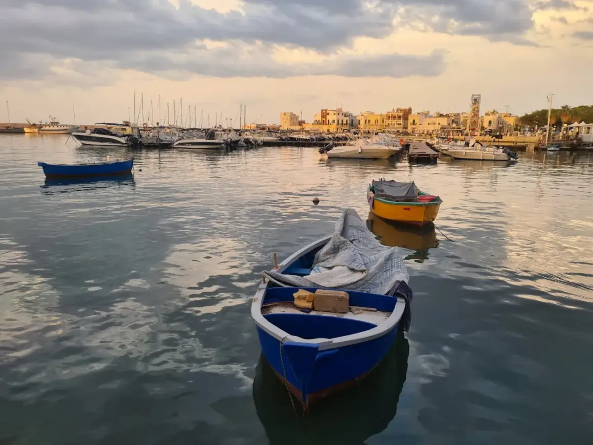 Barche nel porto al tramonto, con la città sullo sfondo. Un'atmosfera di pace e contemplazione, quasi un soffio di **santo spirito** sul mare calmo.