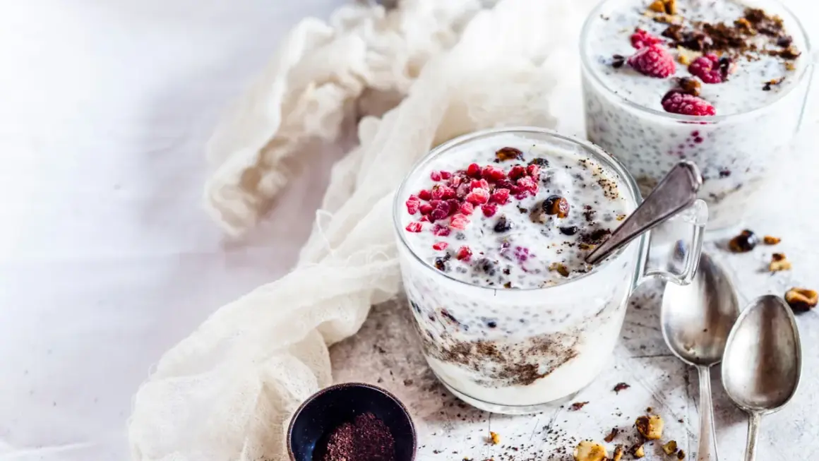 Due bicchieri di yogurt con semi di chia, lamponi e granella di nocciole. Un dessert sano e gustoso.