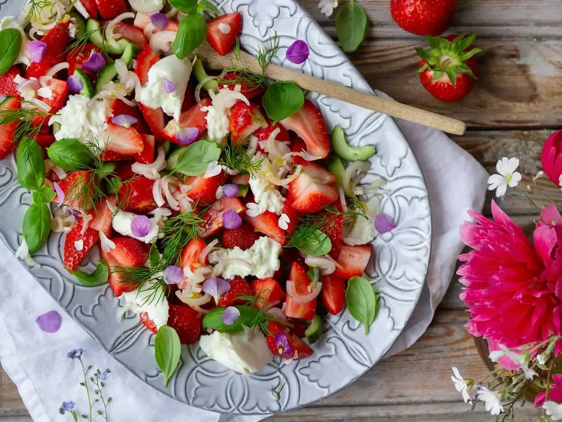 En härlig somrig sallad med jordgubbar, mozzarella, gurka och färska örter, dekorerad med ätbara blommor.