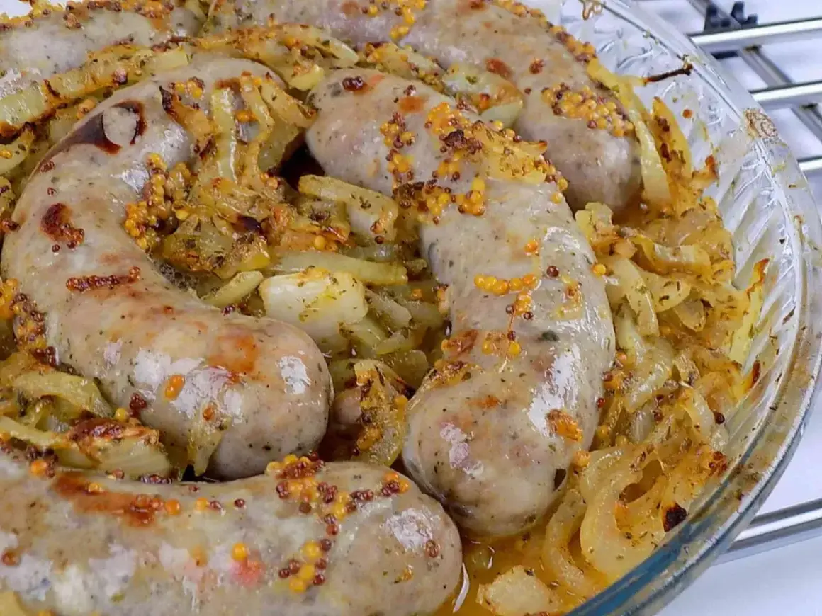Pyszna biała kiełbasa pieczona w cebuli i musztardzie, z chrupiącymi ziarnami gorczycy. Aromatyczne danie w szklanej formie.