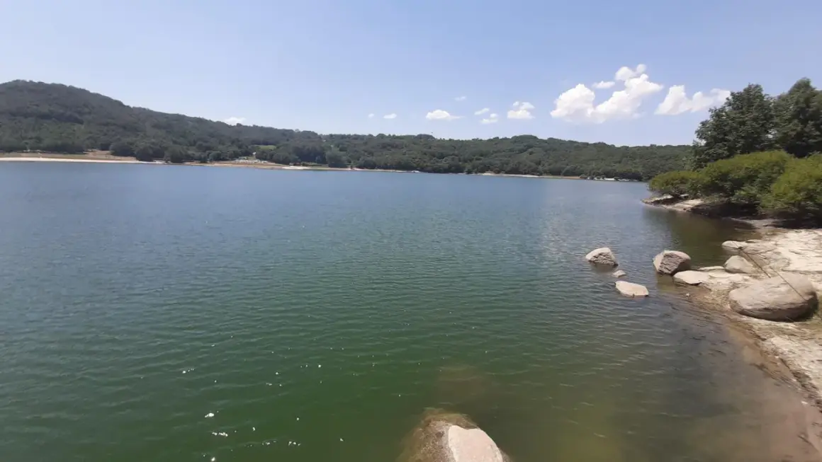 Un lago sereno rodeado de colinas verdes, con rocas en la orilla. Un lugar perfecto para desconectar en Xares a Veiga.