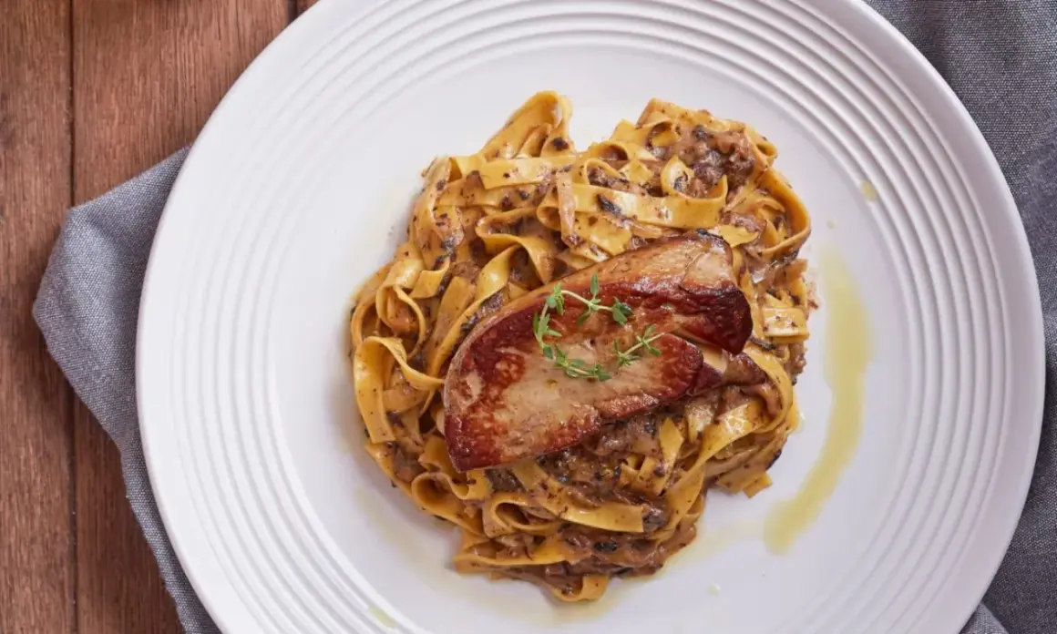 Pasta con foie gras, un plato gourmet con un trozo dorado de foie gras sobre una cama de fettuccine cremoso.
