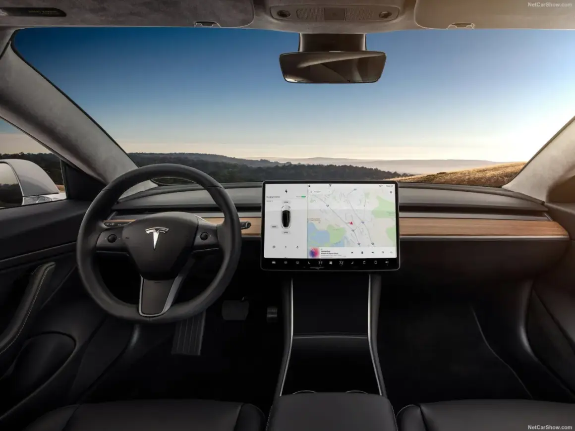 Wnętrze Tesla Model S z dużym ekranem dotykowym, kierownicą i widokiem na krajobraz za oknem.