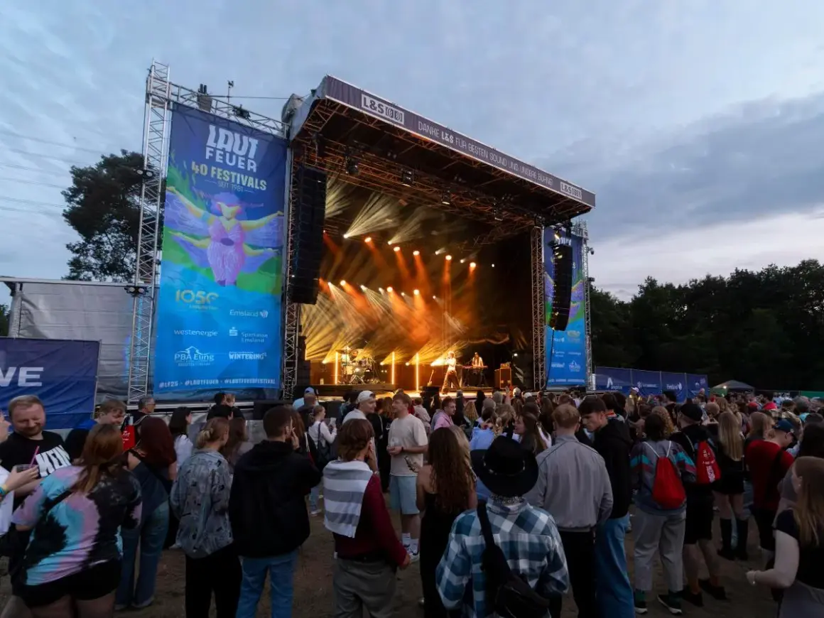 Menschenmenge vor einer Bühne beim lautfeuer festival. Scheinwerfer beleuchten die Bühne, auf der Musiker spielen.