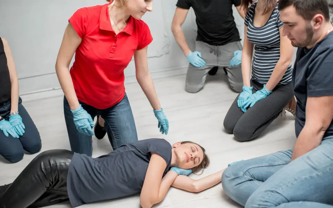Erste-Hilfe-Kurs: Eine Frau in Rot zeigt die stabile Seitenlage. Ein Merksatz hilft beim Erinnern.