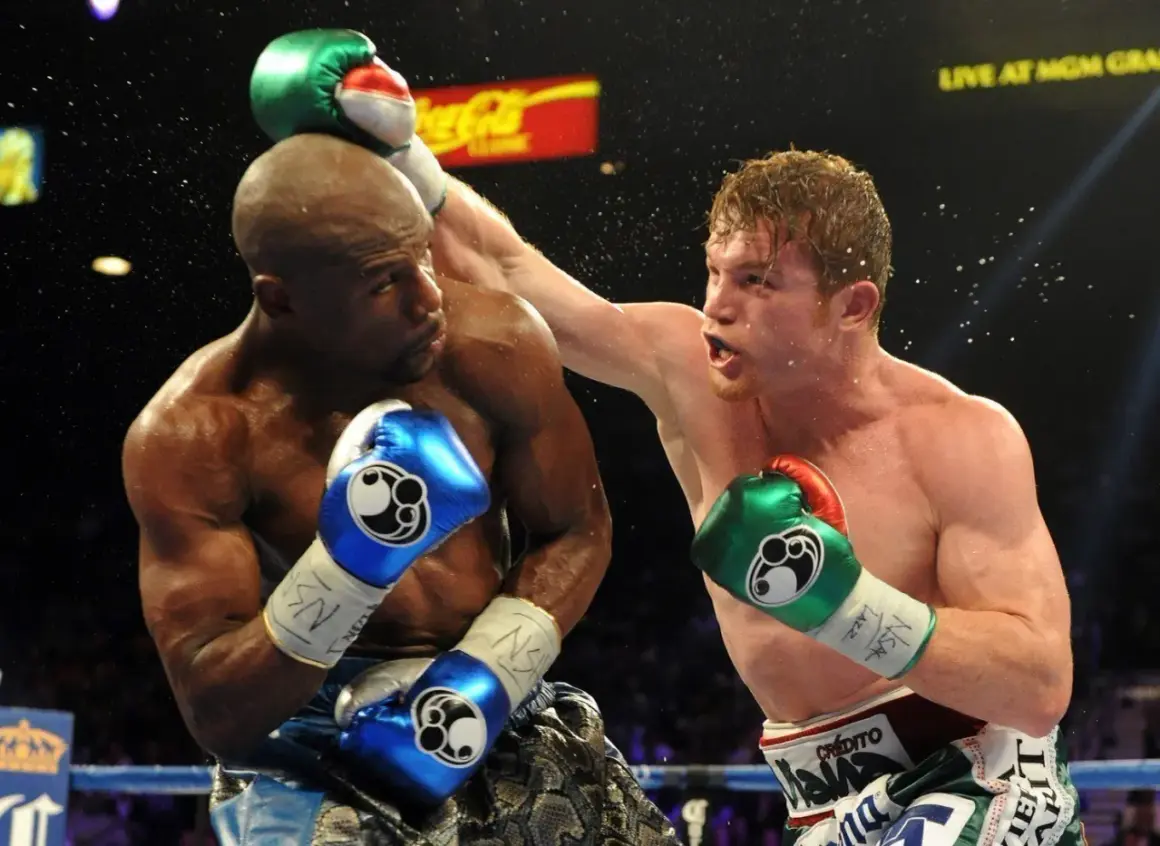 Two boxers exchange blows, one with a blue boxing guard, the other with a green one. Sweat flies as they fight.