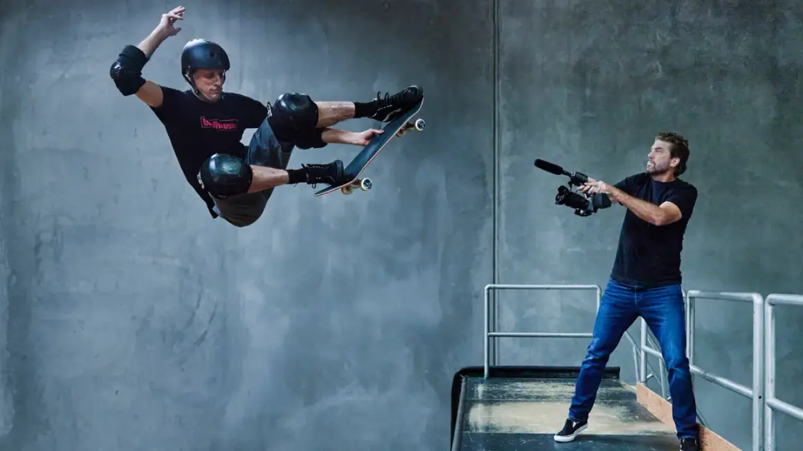 Tony Hawk w locie na deskorolce, filmowany przez operatora kamery.
