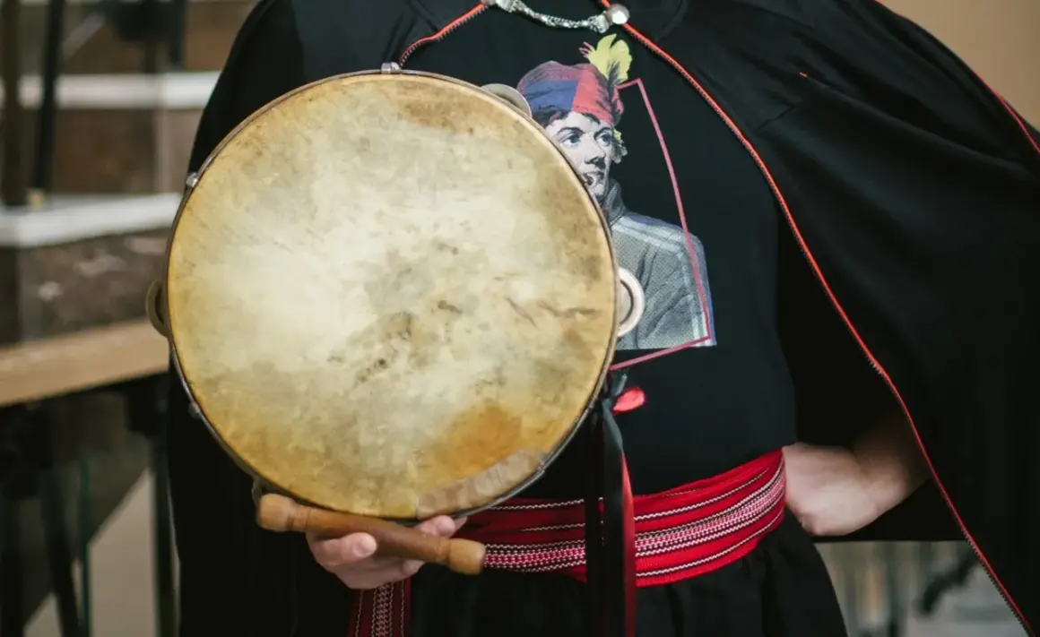 Mateusz Dobrowolski trzyma bębenek. Na czarnej koszulce widnieje wizerunek mężczyzny w kolorowej czapce.