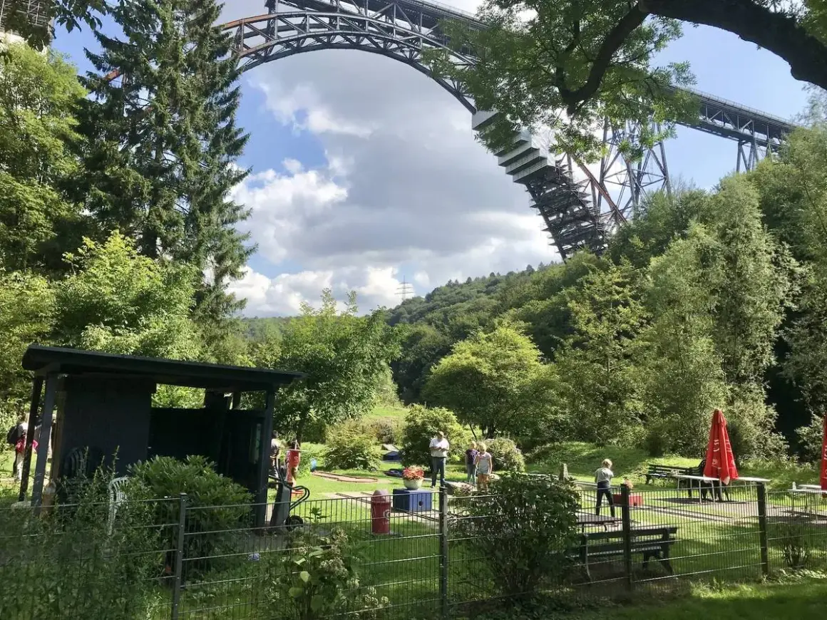 Familien genießen ein **adventure minigolf nrw** unter der imposanten Eisenbahnbrücke.