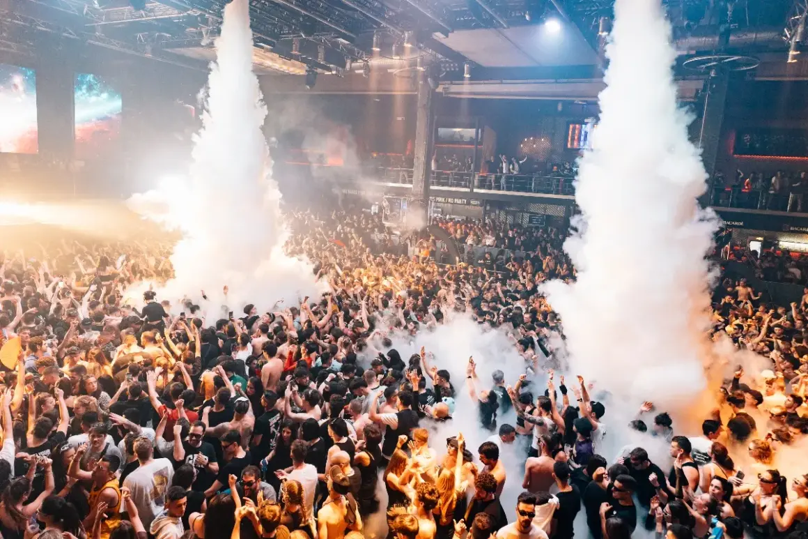 Folla in delirio in una discoteca, tra fumo e luci. Un'atmosfera elettrizzante che fa pensare alle migliori discoteche Madrid.