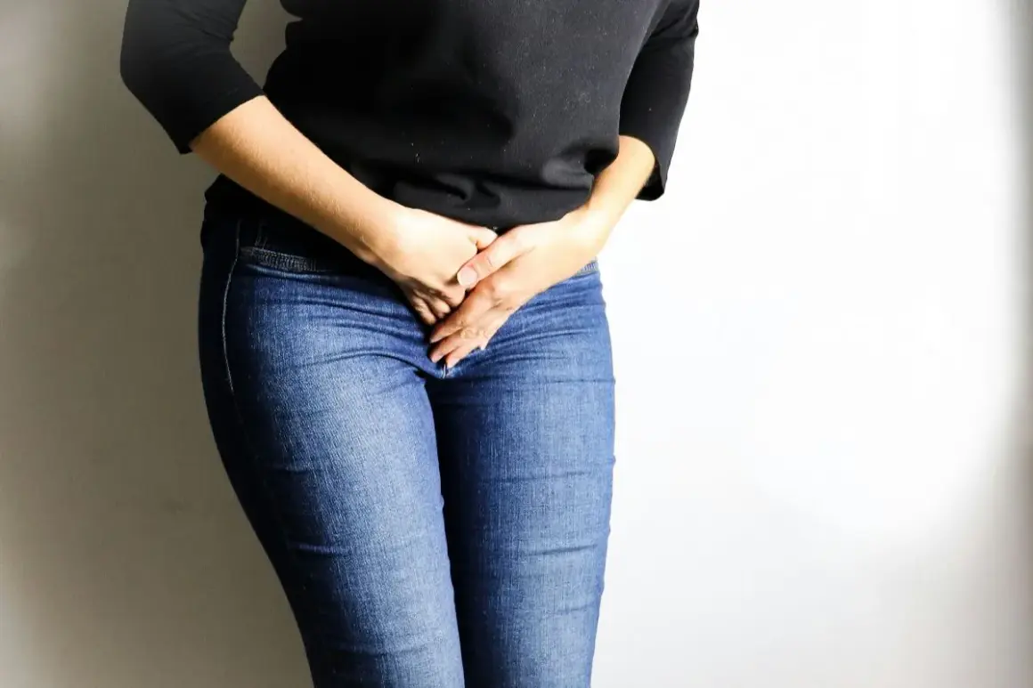 Femme en jean tenant ses mains sur son bas-ventre, évoquant une gêne, peut-être liée à une bronchite et une fuite urinaire.