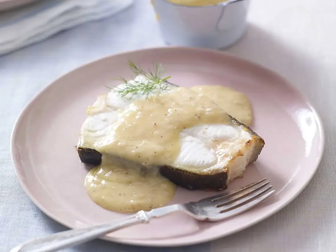 En bit fisk täckt med krämig beurre blanc-sås, garnerad med dill, serveras på en rosa tallrik med en gaffel.