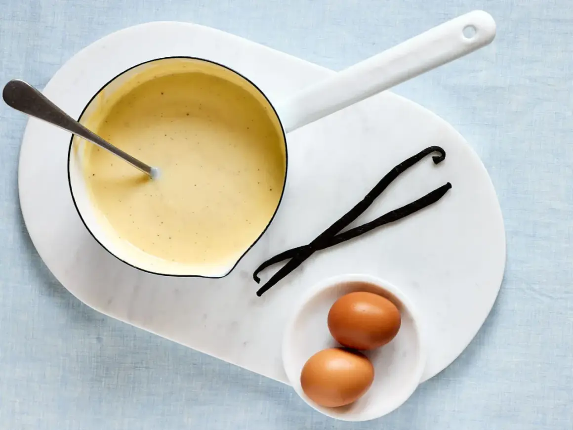 Zutaten für vanillesauce selber machen: ein Topf mit cremiger Sauce, zwei Eier und zwei Vanilleschoten.
