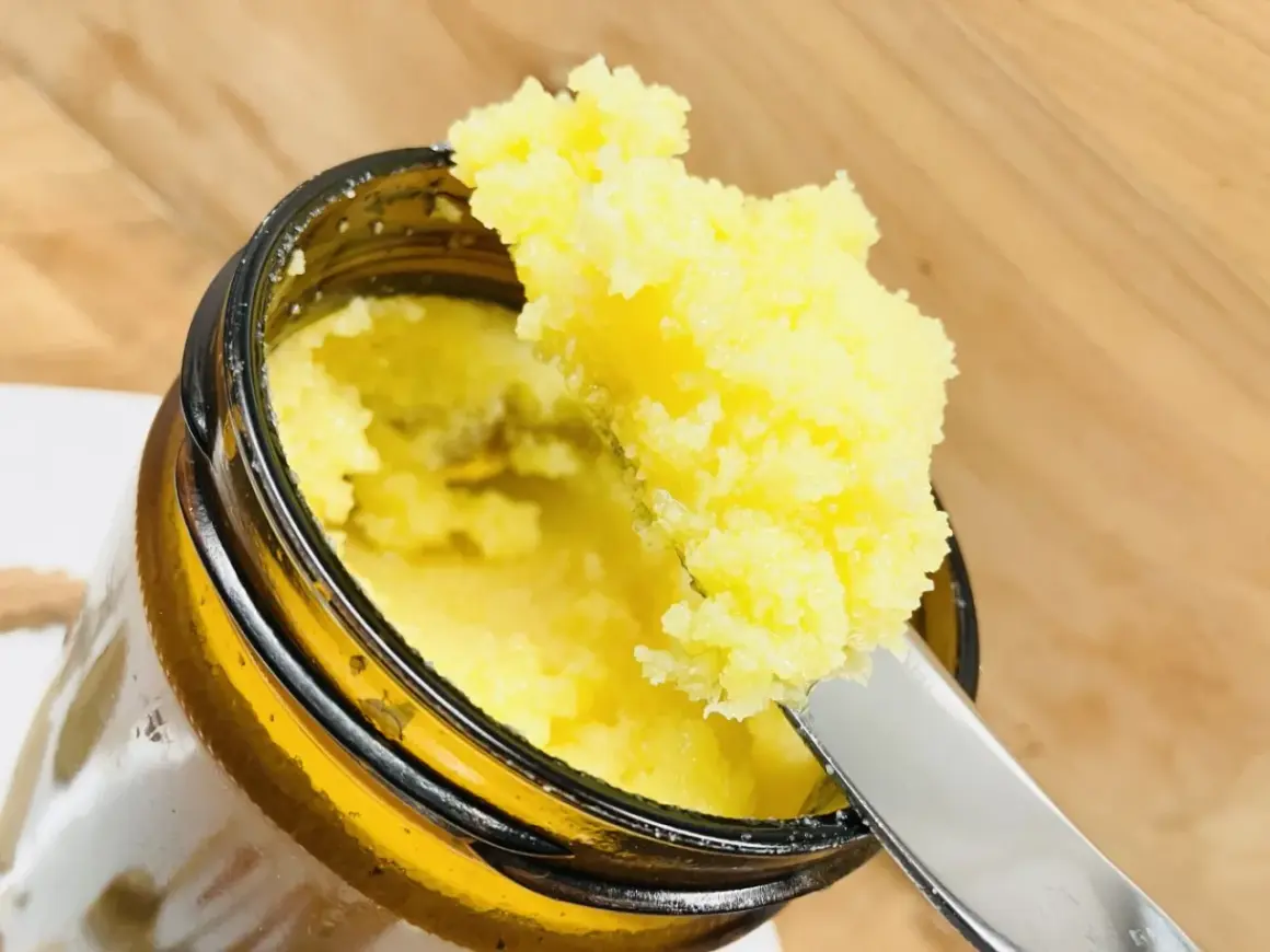 Ein Löffel hebt goldgelbes Ghee Butter aus einem Glas. Was ist Ghee Butter? Ein geklärte Butter, ideal zum Kochen.