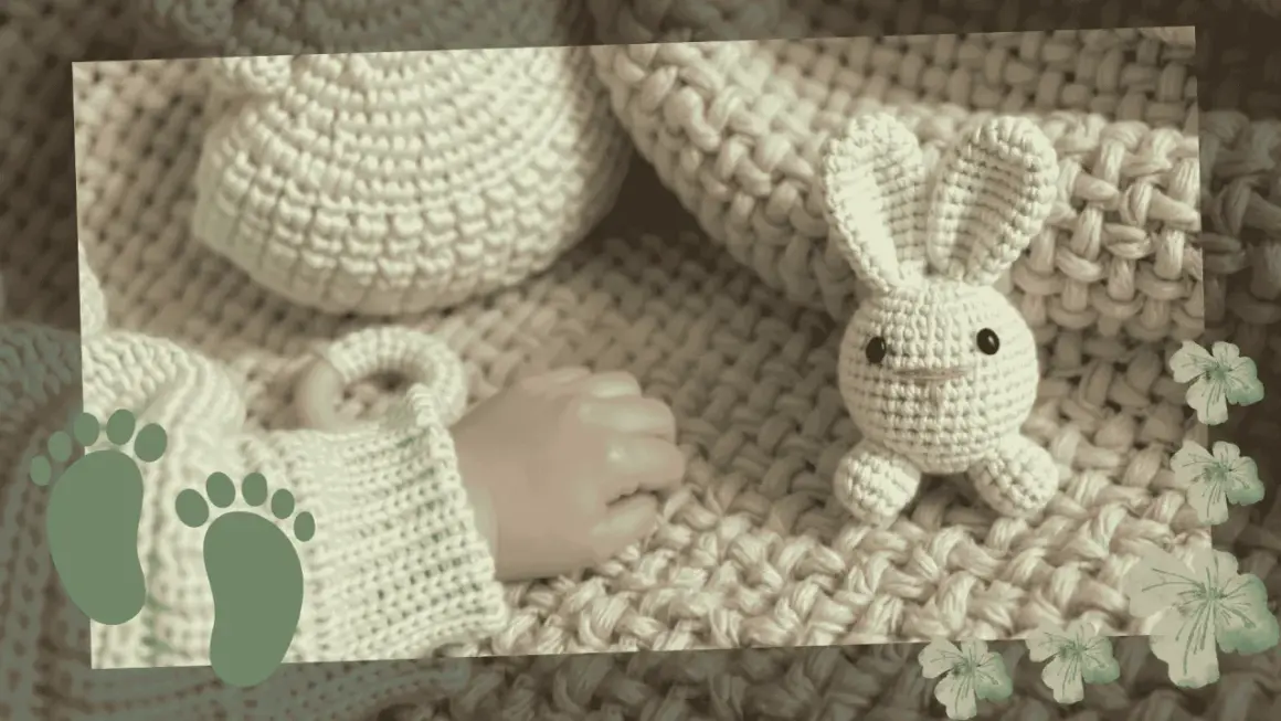 Crocheted bunny and baby's hand on a knitted blanket with baby footprints.